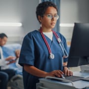 Nurse-on-Computer-with-Doctor-and-Patient-in-Background