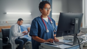 Nurse-on-Computer-with-Doctor-and-Patient-in-Background