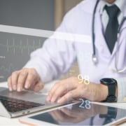 Doctor working on laptop with medical dashboard ECG, SpO2, and vital signs real-time healthcare monitoring. Advanced health technology data screen, telemedicine and smart hospital systems.