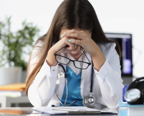 critical care physician burnout. Tired doctor sitting at table and holding glasses in clinic. Treatment of critical patients concept